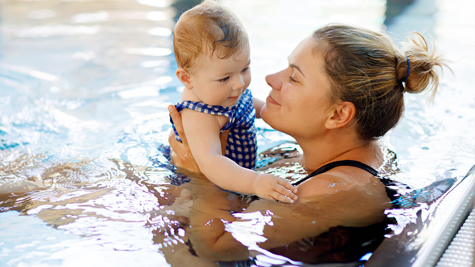 Mutter schwimmt mit kleiner Tochter im Schwimmbecken