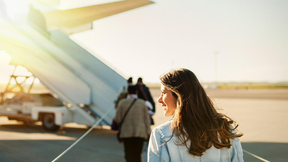 Junge Frau läuft zum Flugzeug während ihr die Sonne ins Gesicht scheint